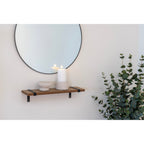 Bougeoirs en ciment gris clair avec une bougie pilier sur une étagère murale en bois sous un miroir rond