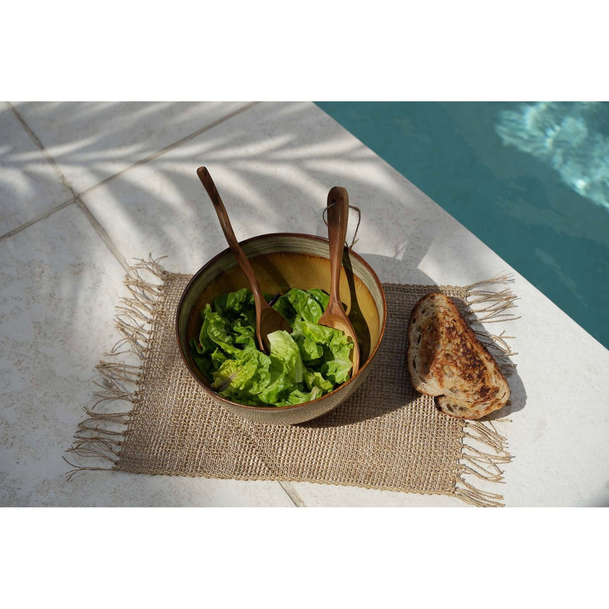Set de table Isey vu de dessus avec un saladier en grès des couverts à salade en bois et du pain grillé