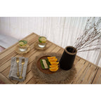 Set de table en jonc de mer sur une table en bois sous une assiette en bois avec des verres et des couverts dorés