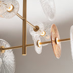 Détail des bras en métal doré mat de la suspension Allure avec les points LED allumés au centre des disques de verre strié