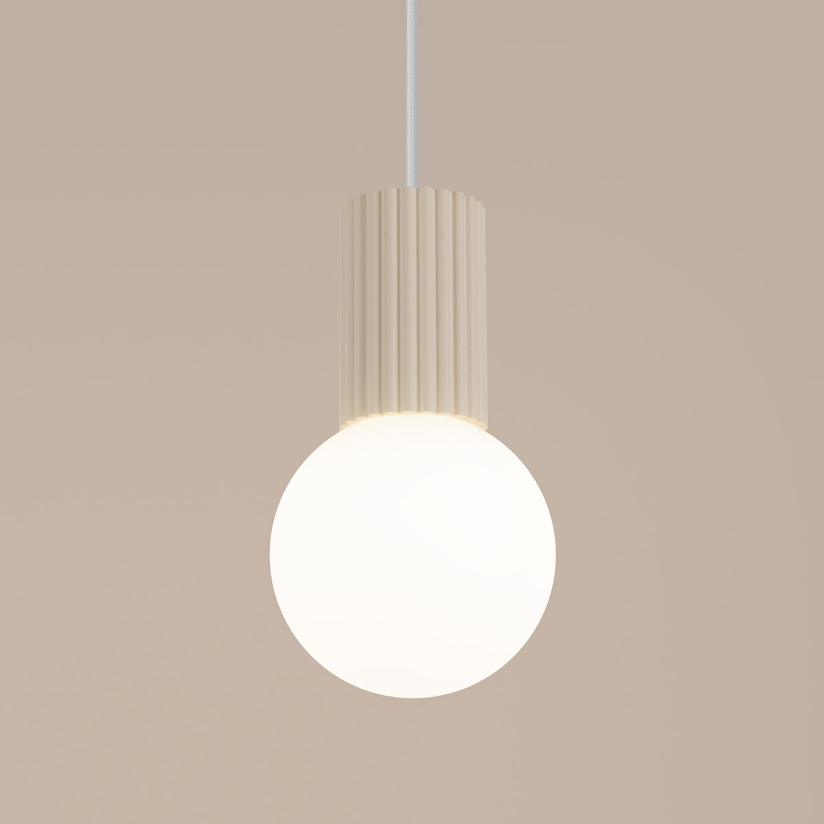 Gros plan de la suspension Halo laque beige allumée avec son culot cannelé au-dessus de la boule opale