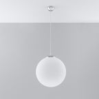 Suspension boule Ugo en verre blanc suspendue sous un plafond blanc devant un mur gris