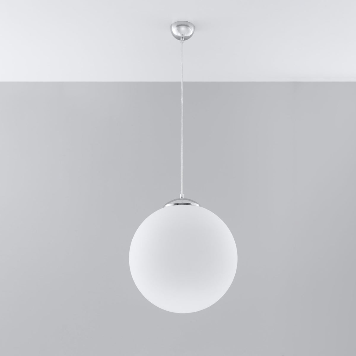 Suspension boule Ugo en verre blanc suspendue sous un plafond blanc devant un mur gris
