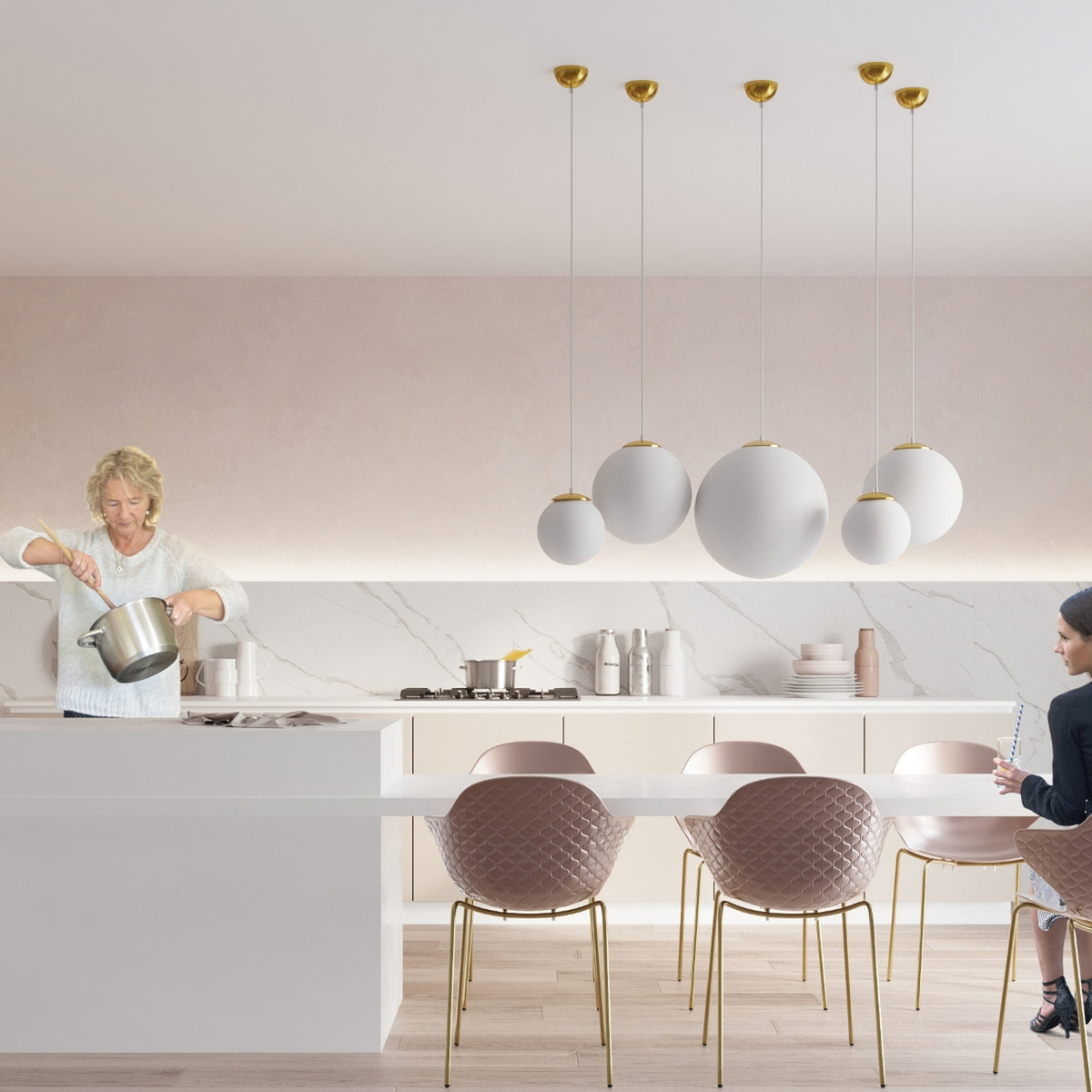 Boules Ugo de plusieurs tailles à coupelles dorées au-dessus d'une table de cuisine avec des chaises rosées
