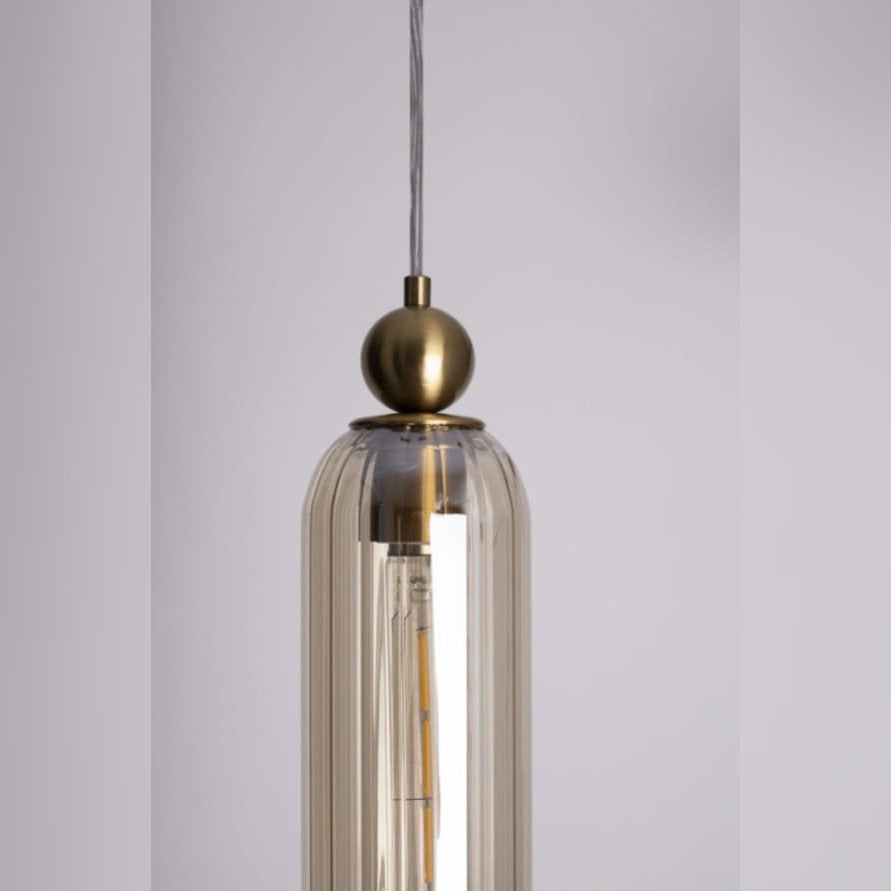Gros plan sur la bille en laiton et le verre ambré strié de la suspension Campanila avec son ampoule à filament