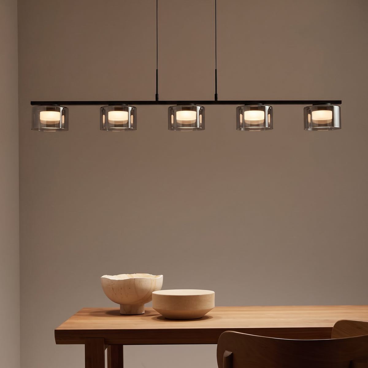 Suspension Cholet rampe LED allumée au-dessus d'une table en bois, avec deux bols en bois posés dessus