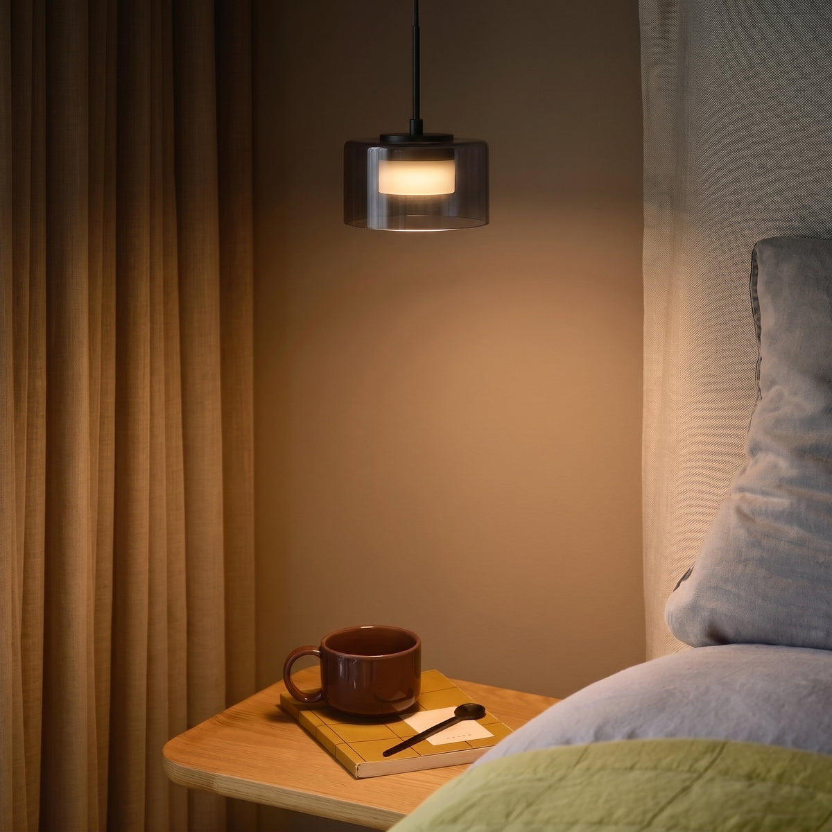 Suspension LED Cholet allumée au-dessus d'une table de chevet en bois, près d'un rideau ocre, d'une tasse brune et d'un carnet jaune