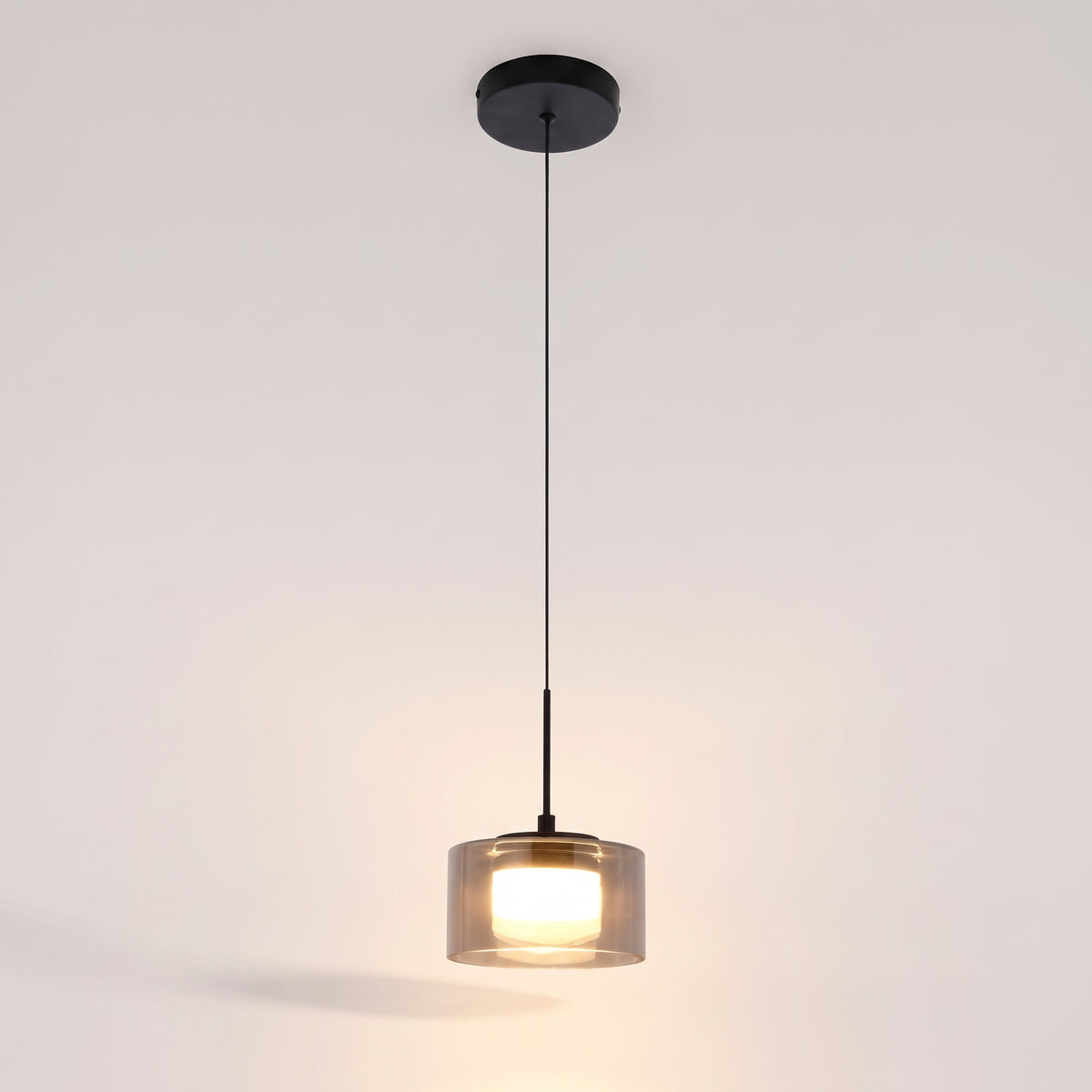 Suspension LED Cholet allumée sur fond clair, cylindre intérieur blanc éclairé sous le verre fumé