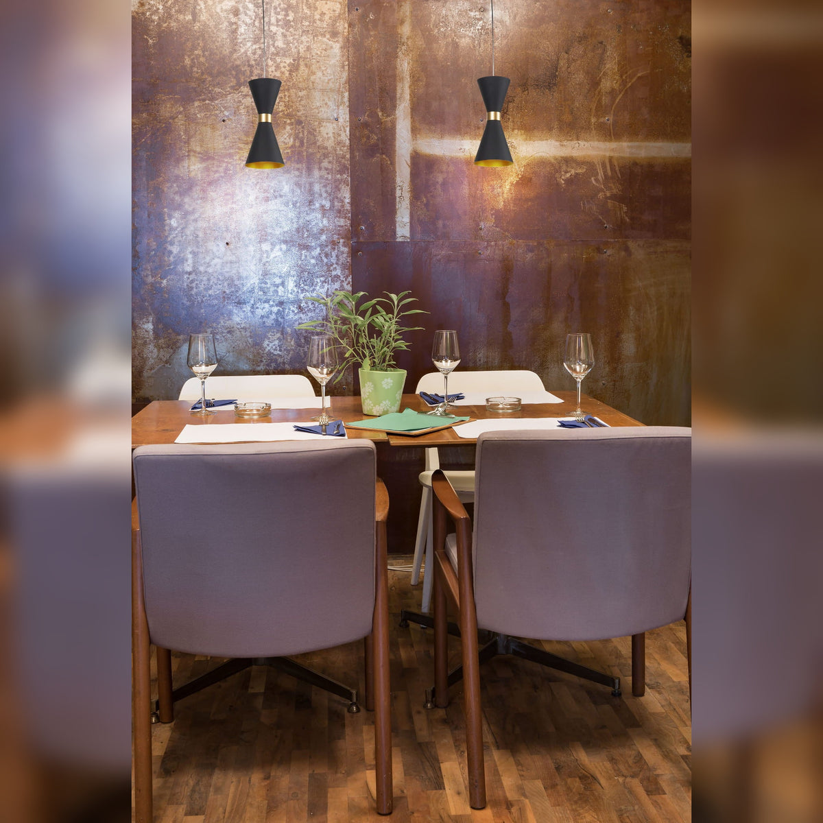 Deux suspensions Cornet noires au-dessus d'une table dressée devant un mur en métal oxydé