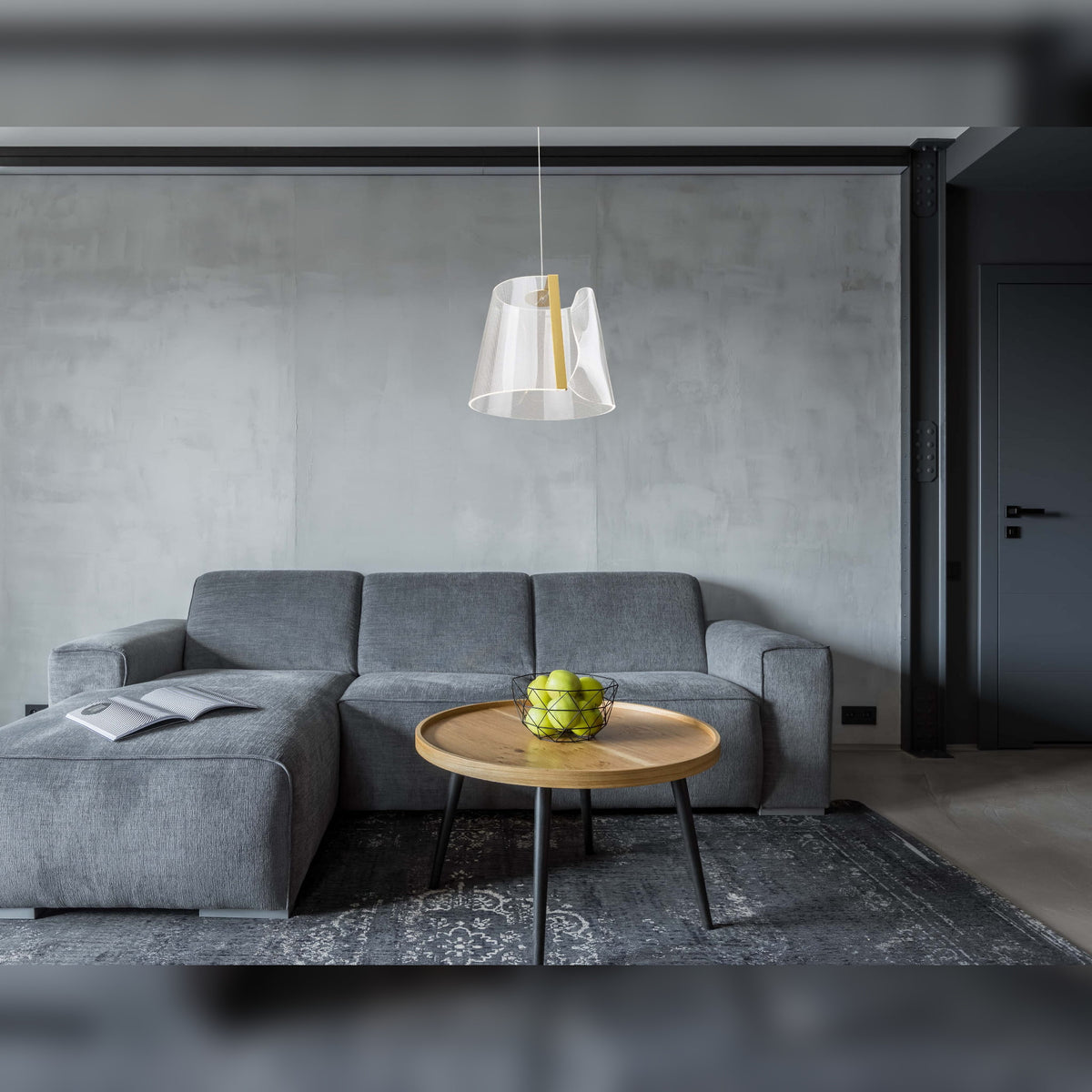 Suspension Seda au-dessus d'une table basse ronde en bois devant un canapé d'angle gris et un mur en béton