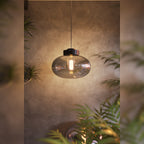 Suspension Moonstone verre fumé et marbre noir allumée devant un mur en béton entre des plantes