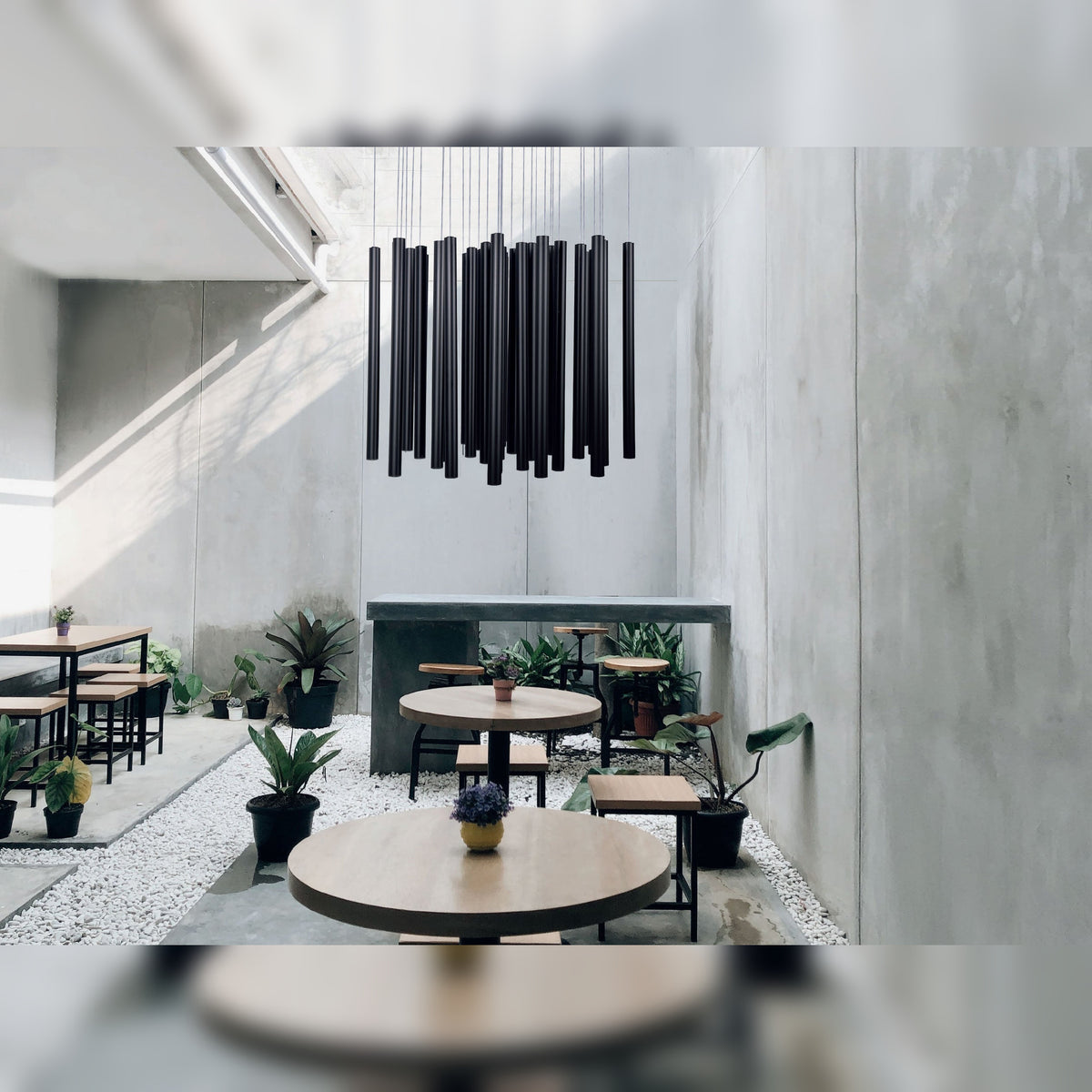 Suspension Organic Métal noir sous un haut plafond dans un café aux murs de béton avec tables rondes en bois