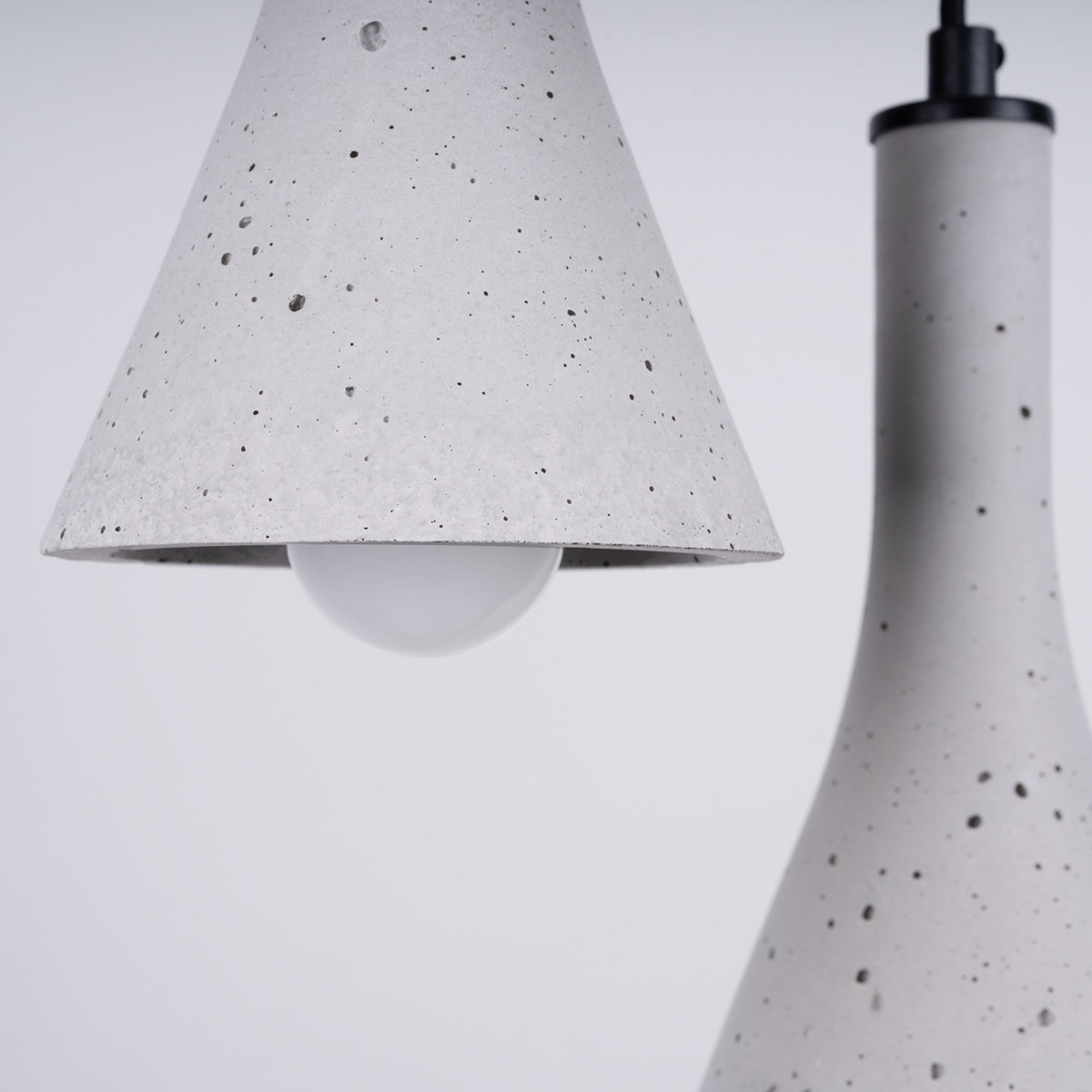 Détail d'un abat-jour Rea en béton gris moucheté avec son ampoule opale et son capuchon noir
