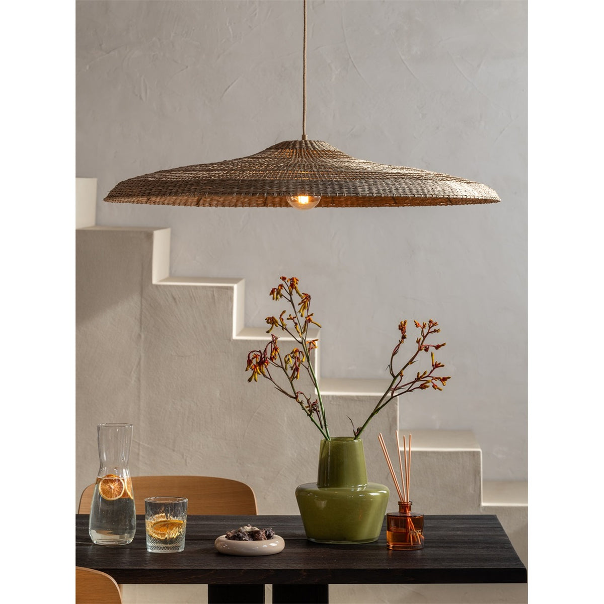 Suspension Santorini allumée au-dessus d'une table en bois sombre devant un escalier