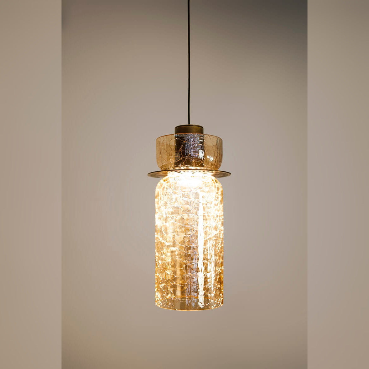 Suspension Signature B allumée sur un mur beige lumière chaude à travers le verre craquelé