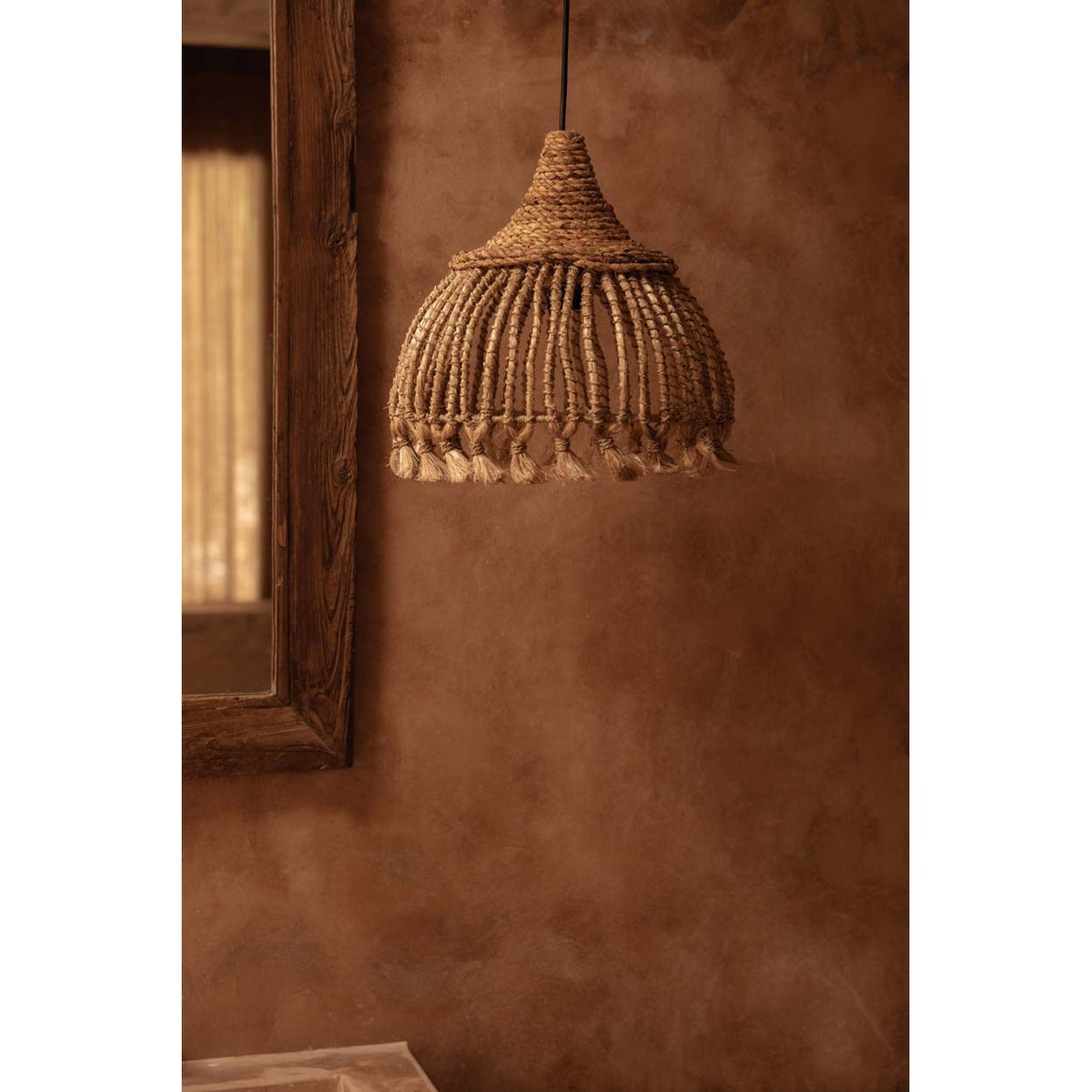 Suspension Tassel en abaca vue de face dans une pièce aux murs bruns près d'un miroir