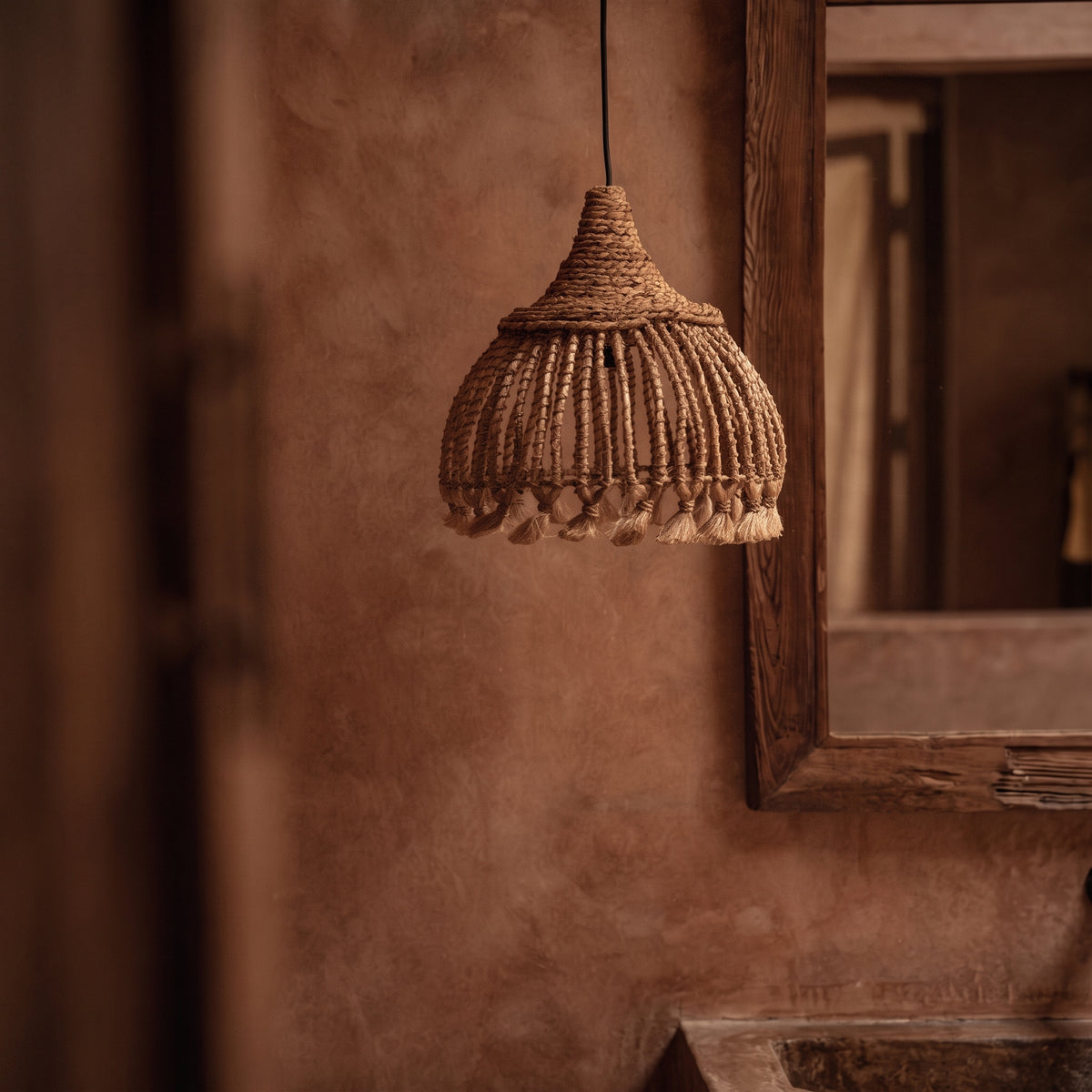 Suspension Tassel en abaca naturel au-dessus d'une vasque, devant un mur terracotta et un miroir en bois