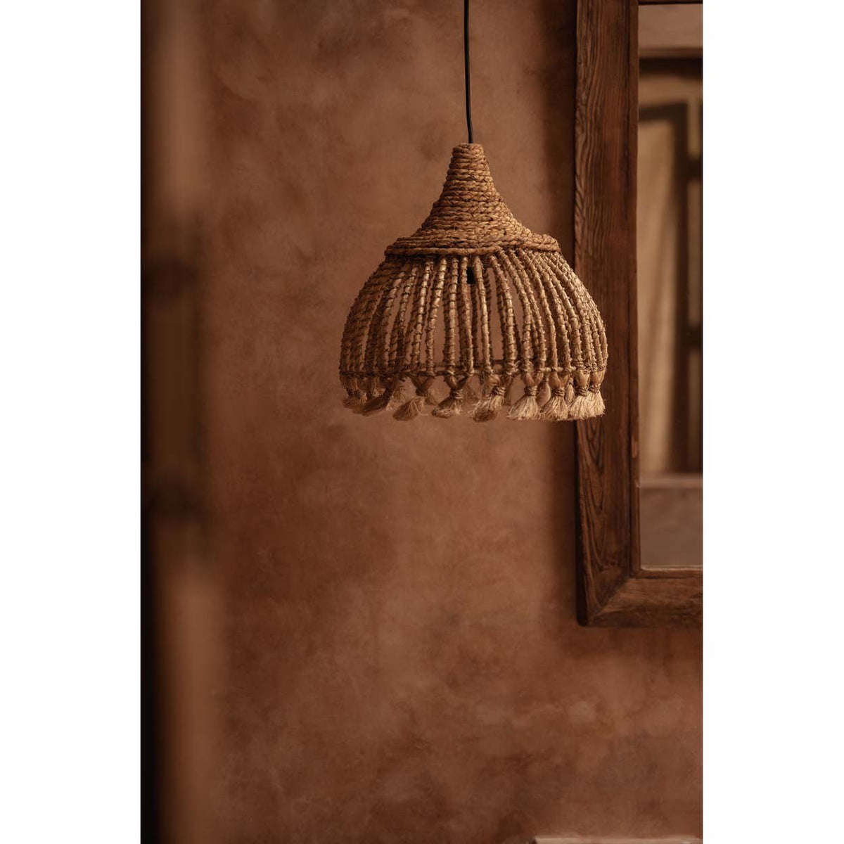Suspension Tassel en abaca accrochée devant un mur terracotta à côté d'un miroir en bois