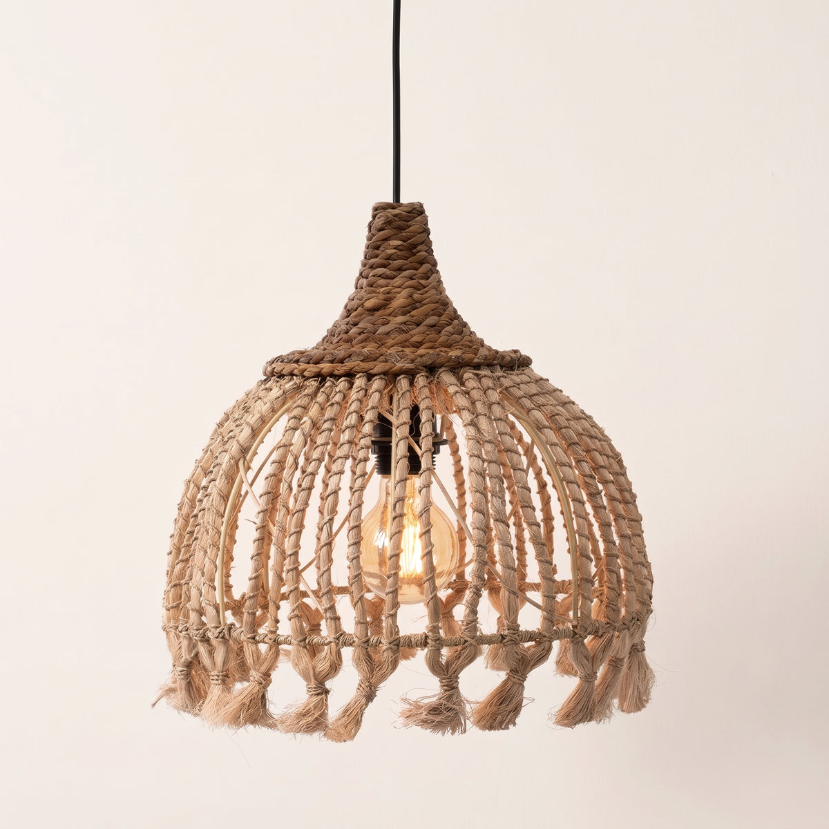 Suspension Tassel en abaca naturel allumée sur fond clair, ampoule à filament visible entre ses cordons tressés à pompons