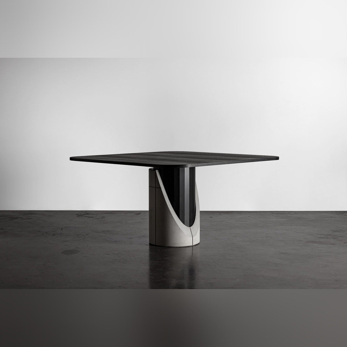 Table à manger Sharp carrée vue de trois quarts dans un studio au sol en béton sombre