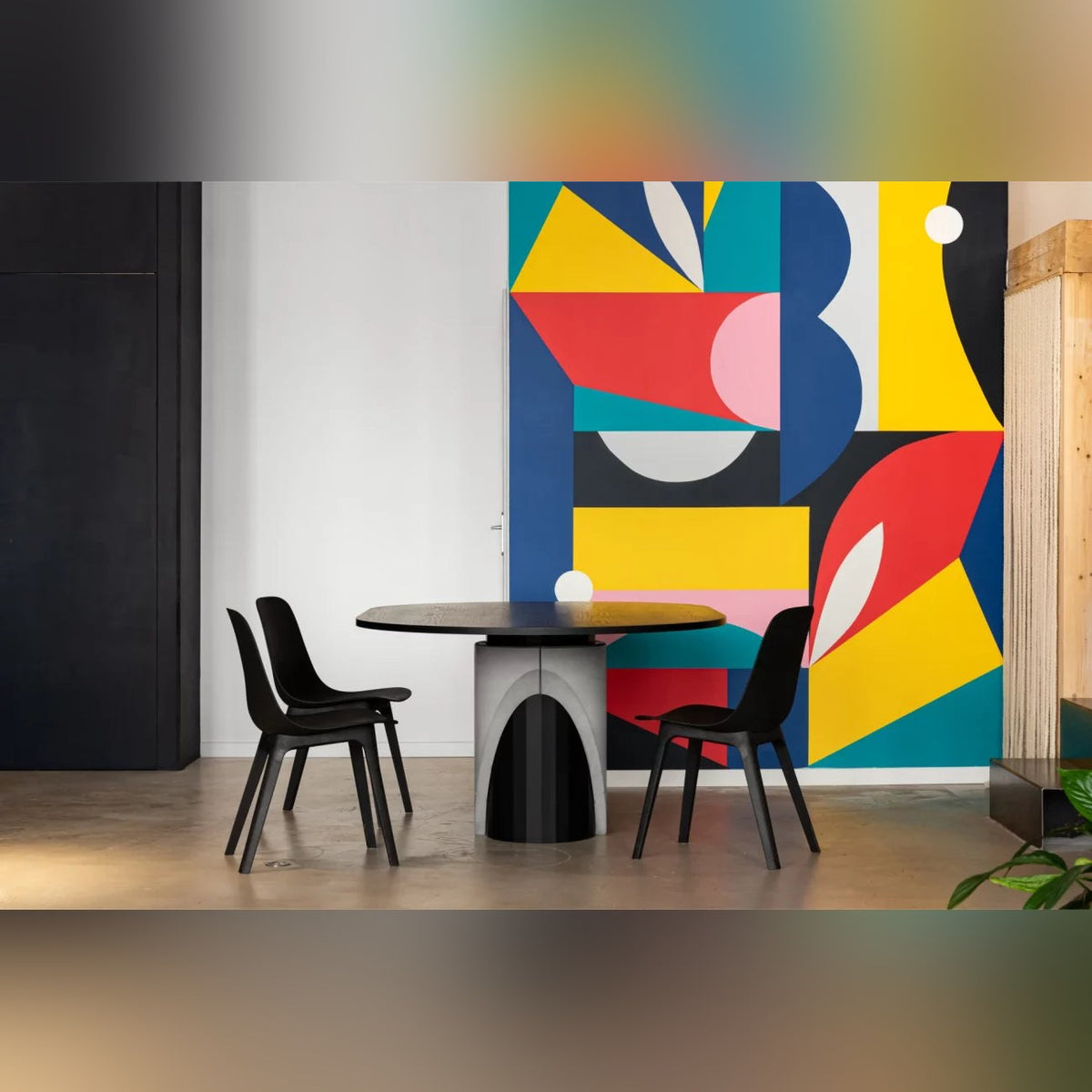Table à manger Sharp entourée de trois chaises noires devant une fresque murale colorée