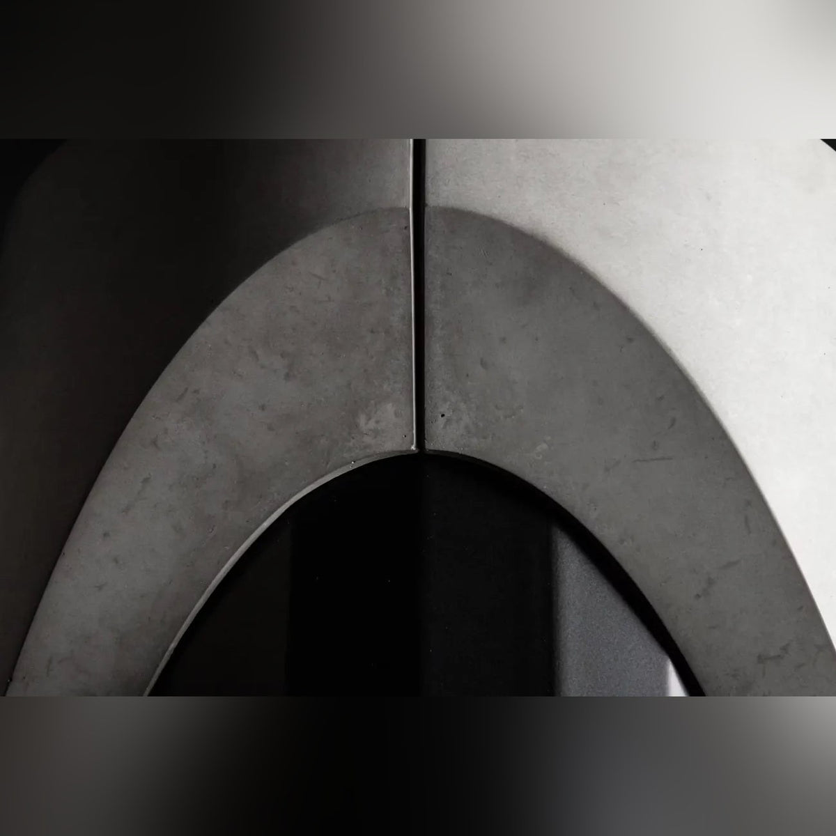 Détail de l'arche formée par les deux demi-lests en béton autour du fût en acier noir de la table Sharp