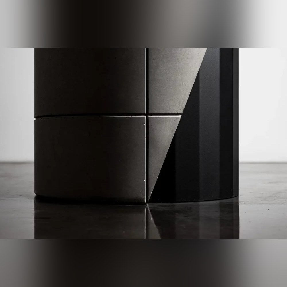 Détail du pied de la table Sharp avec ses demi-lests en béton et la découpe en biais sur le fût en acier noir