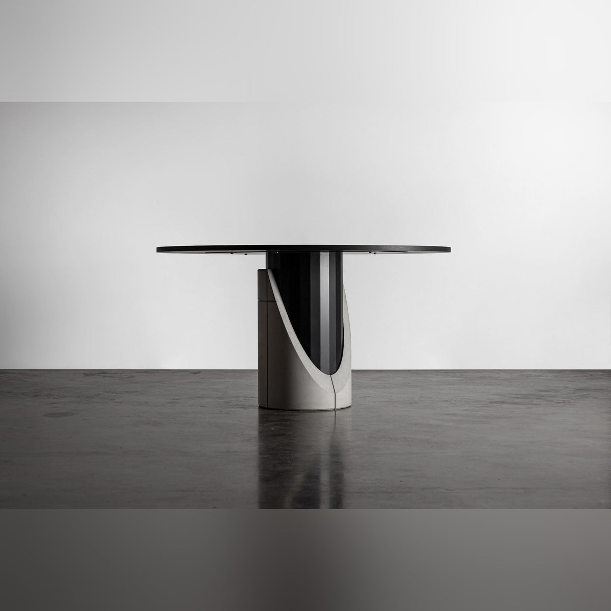 Table à manger Sharp ronde et la courbe de son lest en béton qui dévoile le fût en acier noir facetté
