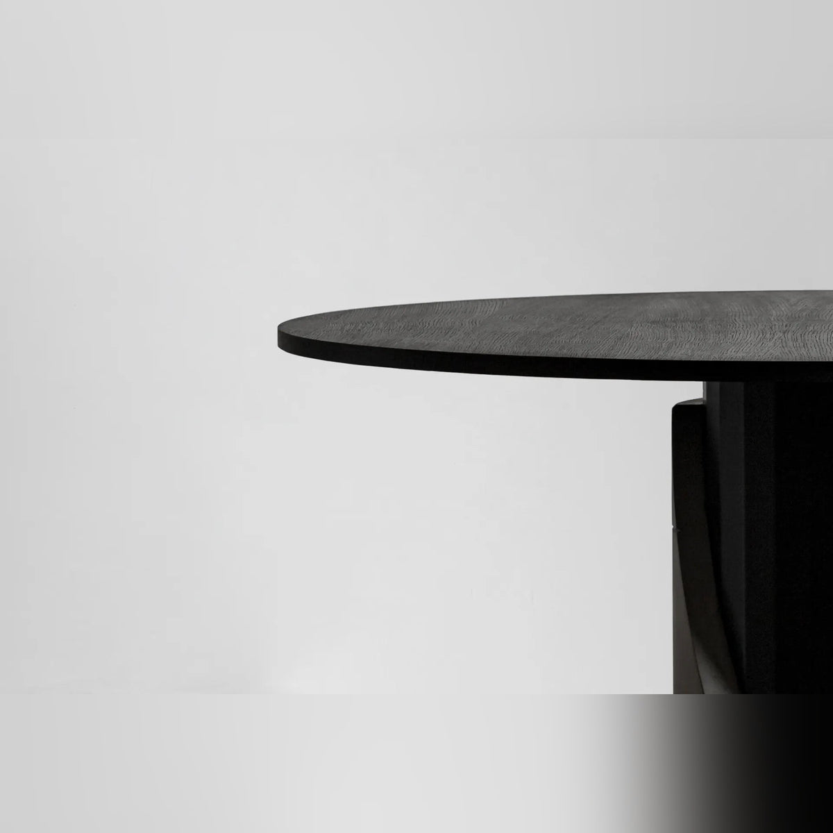 Détail du bord du plateau rond plaqué chêne teinté noir de la table Sharp au-dessus de son pied