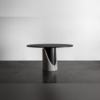 Table à manger Sharp ronde posée sur un sol en béton sombre devant un mur blanc