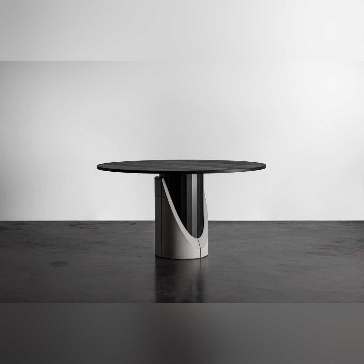 Table à manger Sharp ronde posée sur un sol en béton sombre devant un mur blanc