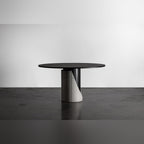 Table à manger Sharp ronde vue de trois quarts avec son lest en béton gris naturel et son fût noir sur un sol en béton