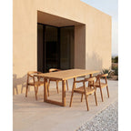 Table à manger Imola en teck sur une terrasse avec quatre fauteuils en teck devant un mur ocre