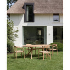Table à manger ovale Kulala entourée de quatre fauteuils à assise tressée devant une maison blanche