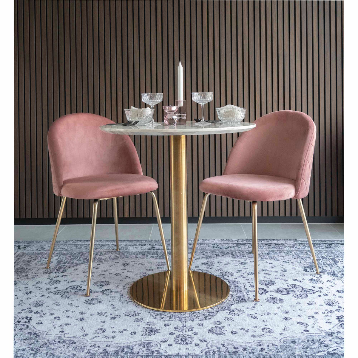 Table Bolzano dressée avec des coupes entre deux chaises en velours rose
