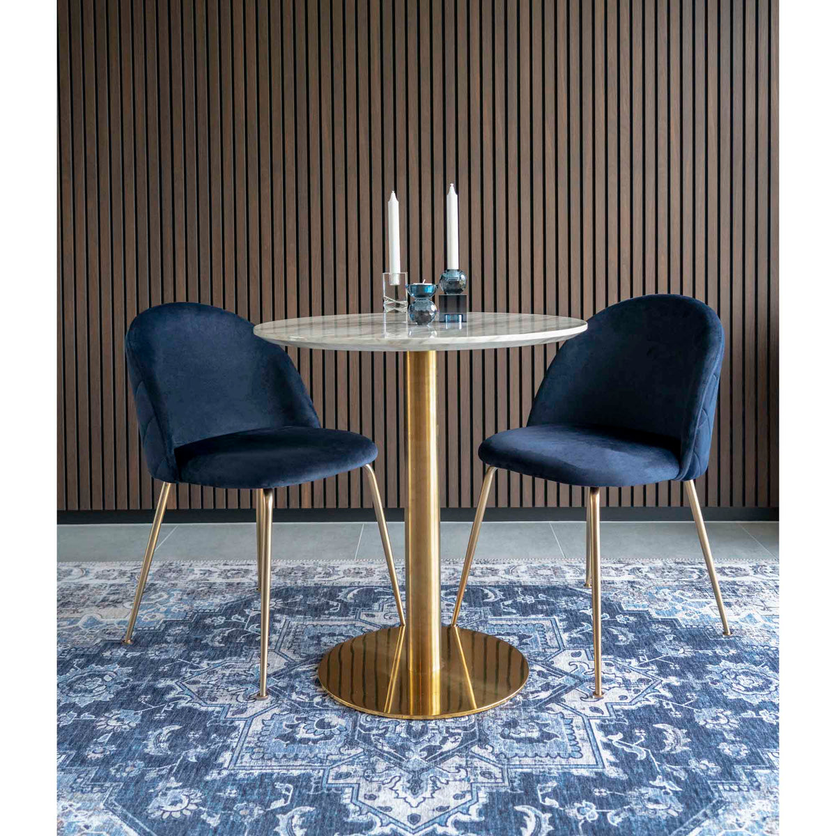 Table Bolzano dressée avec deux bougies entre deux chaises en velours bleu nuit