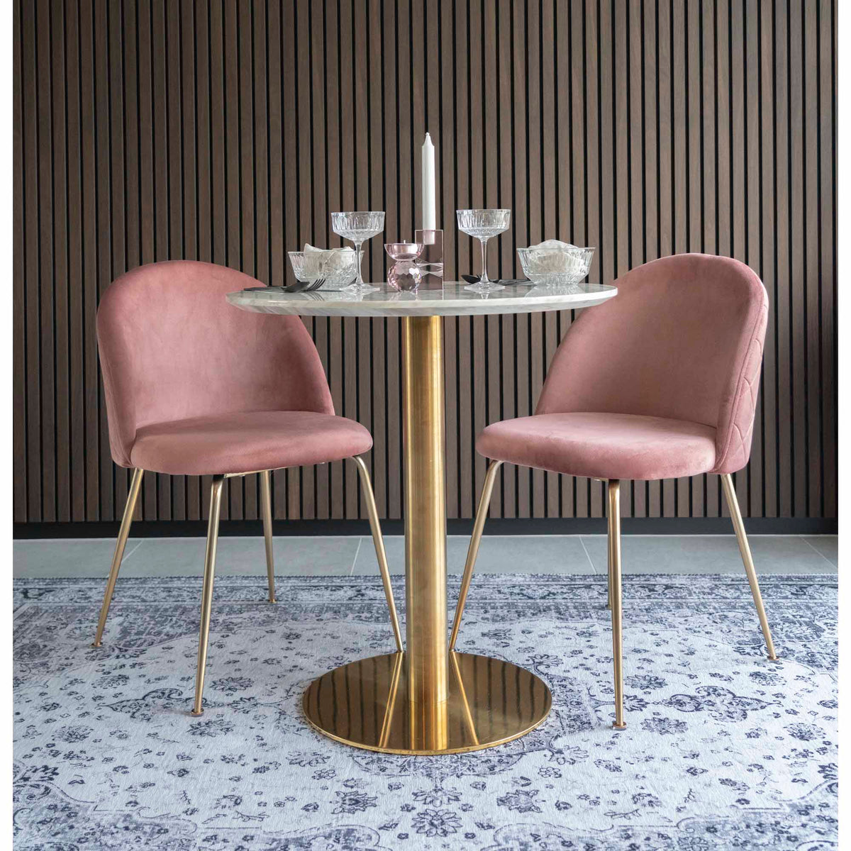 Table Bolzano dressée avec une bougie et des coupes entre deux chaises en velours rose