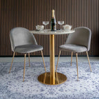 Table Bolzano dressée avec une bouteille et des coupes entre deux chaises en velours gris