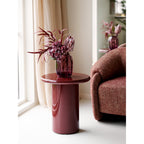 Table d'appoint Otago bordeaux en situation salon avec vase fleurs roses et fauteuil tweed