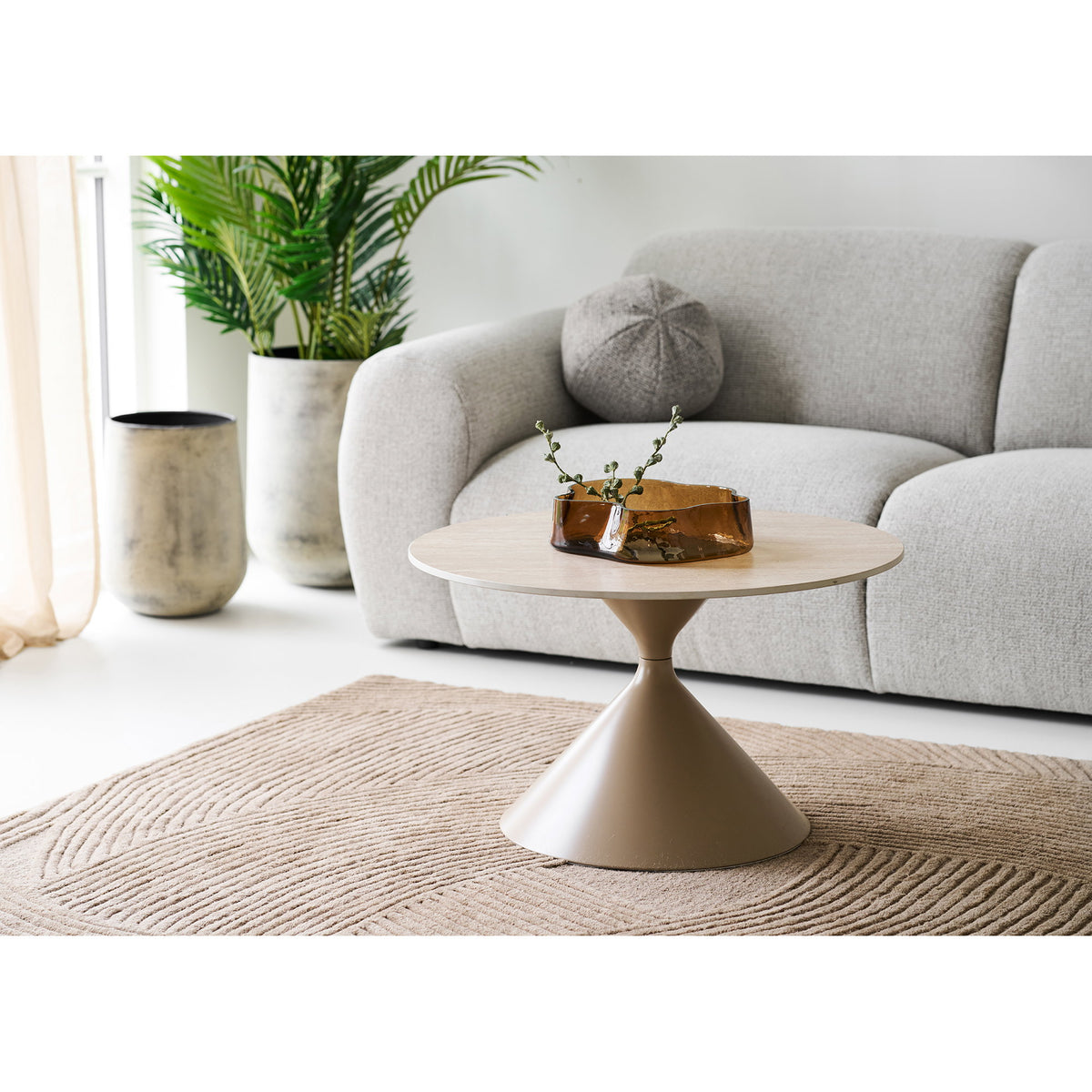 Table basse Annecy devant un canapé gris clair avec une coupe en verre ambré posée sur le plateau
