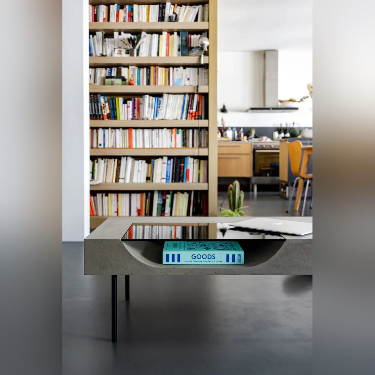 Table basse Curb en béton avec un ordinateur portable posé sur le verre et un livre rangé dans le creux