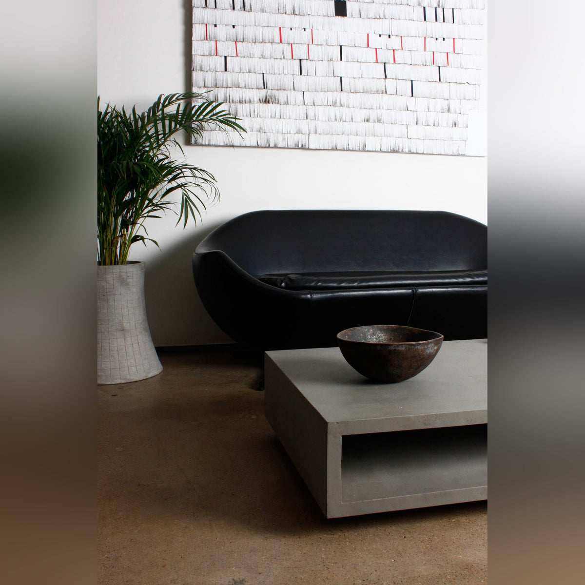 Table basse Monobloc en béton dans un salon avec une coupe en métal patiné et un canapé noir