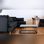 Table basse Perspective en béton vue par le petit côté devant un canapé d'angle noir sur un parquet