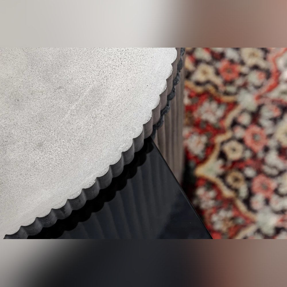 Vue rapprochée du bord cannelé du capot en béton au-dessus du plateau en verre teinté de la table basse Strut carrée