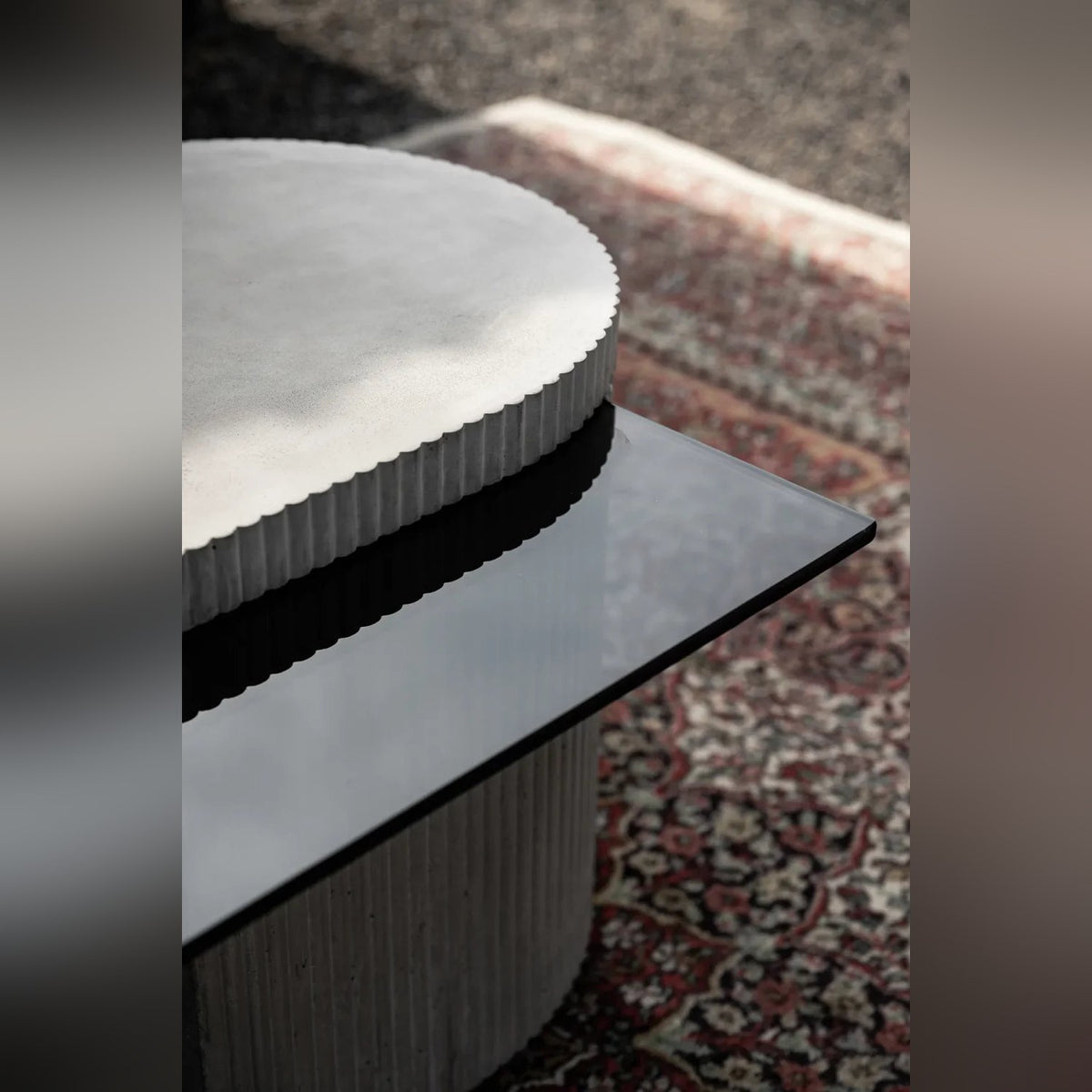 Détail du capot en béton aux bords cannelés posé sur le plateau en verre teinté de la table basse Strut carrée