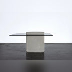 Table basse Strut carrée vue par sa face plane non cannelée en béton gris naturel avec plateau en verre gris sombre sur un sol sombre