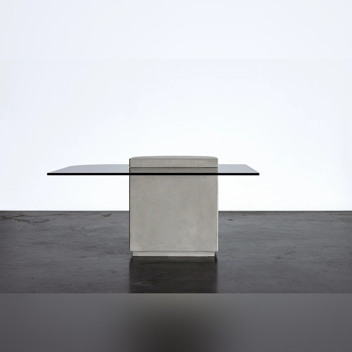 Table basse Strut carrée vue par sa face plane non cannelée en béton gris naturel avec plateau en verre gris sombre sur un sol sombre