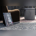 Table basse Strut carrée en arrière-plan d'un fauteuil marron et d'un livre posé sur le gravier