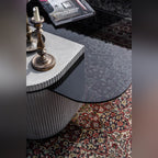Vue plongeante sur la table basse Strut carrée avec bougeoirs en laiton sur le capot en béton cannelé et livre sur le verre teinté