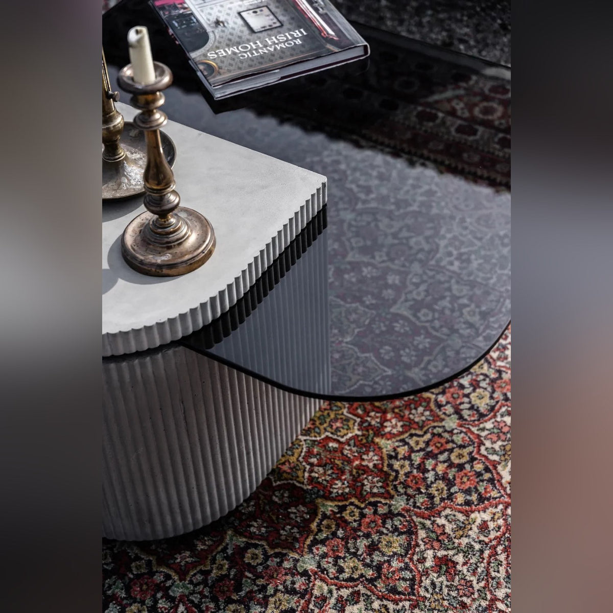Vue plongeante sur la table basse Strut carrée avec bougeoirs en laiton sur le capot en béton cannelé et livre sur le verre teinté